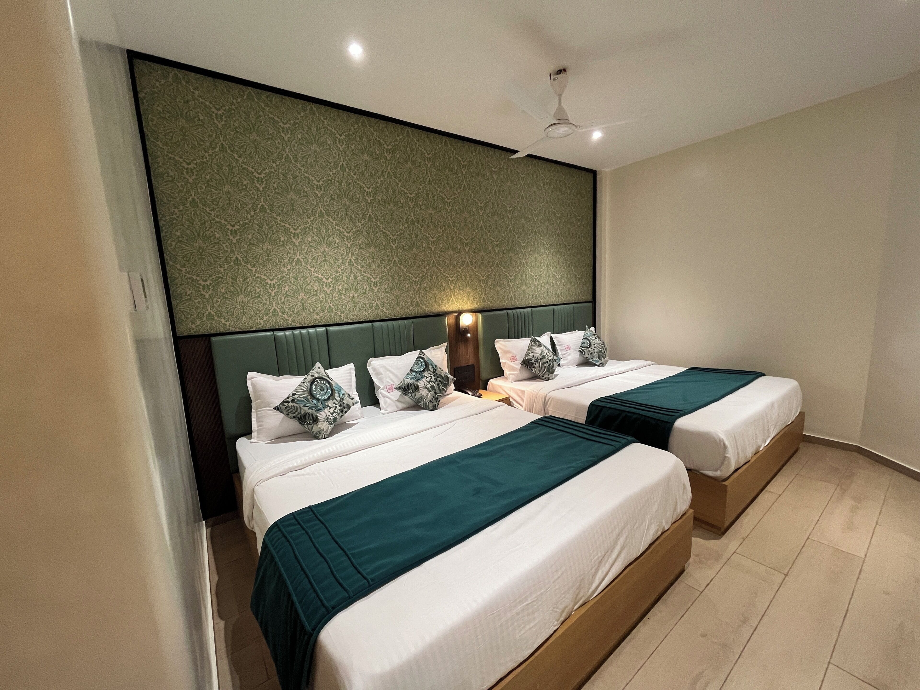 A hotel room with two beds, a green headboard, and a patterned wall.