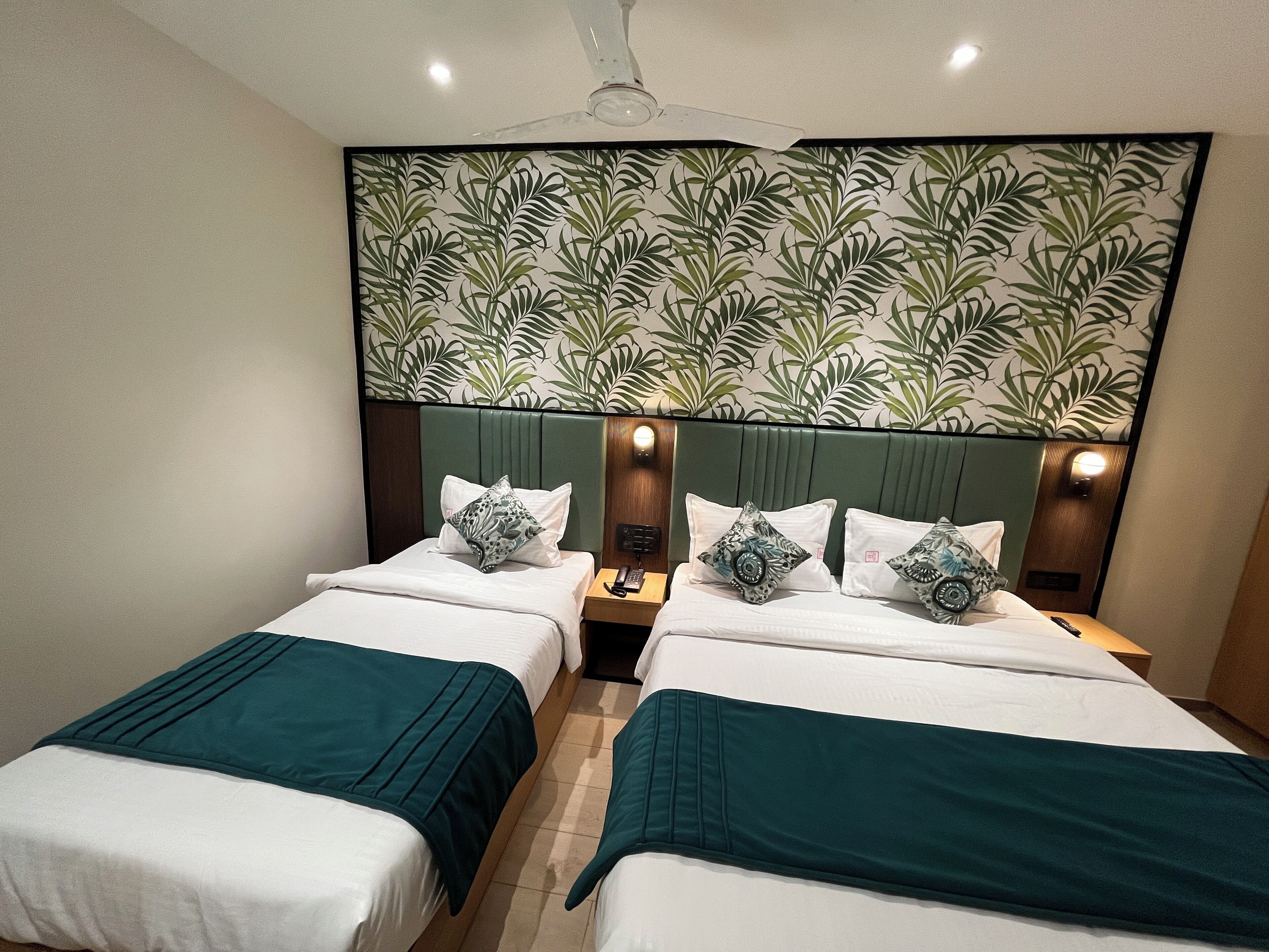 Une chambre d’hôtel avec deux lits, une tête de lit verte et un mur orné d’un motif végétal.