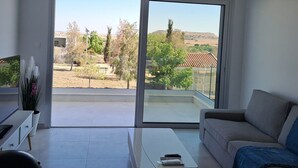 Una sala de estar moderna con un amplio ventanal corredera que da a un balcón, un sofá, una mesa de centro y un televisor sobre un mueble.