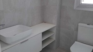 Un baño con lavamanos, inodoro y estantería blancos.
