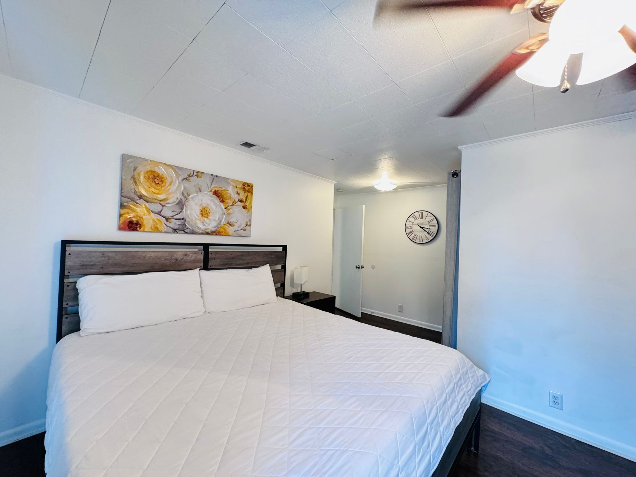 A bedroom with a bed, a ceiling fan, a clock, and a door.