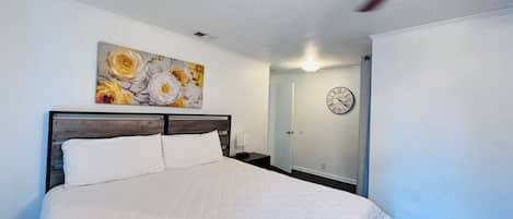 A bedroom with a bed, a ceiling fan, a clock, and a door.