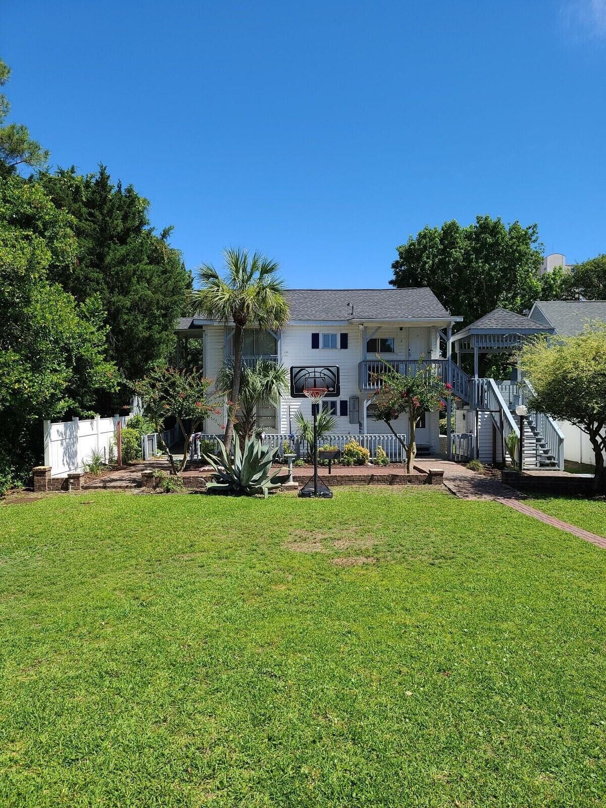 A large, single-story house with a front yard, a basketball hoop, and a staircase leading to a porch.