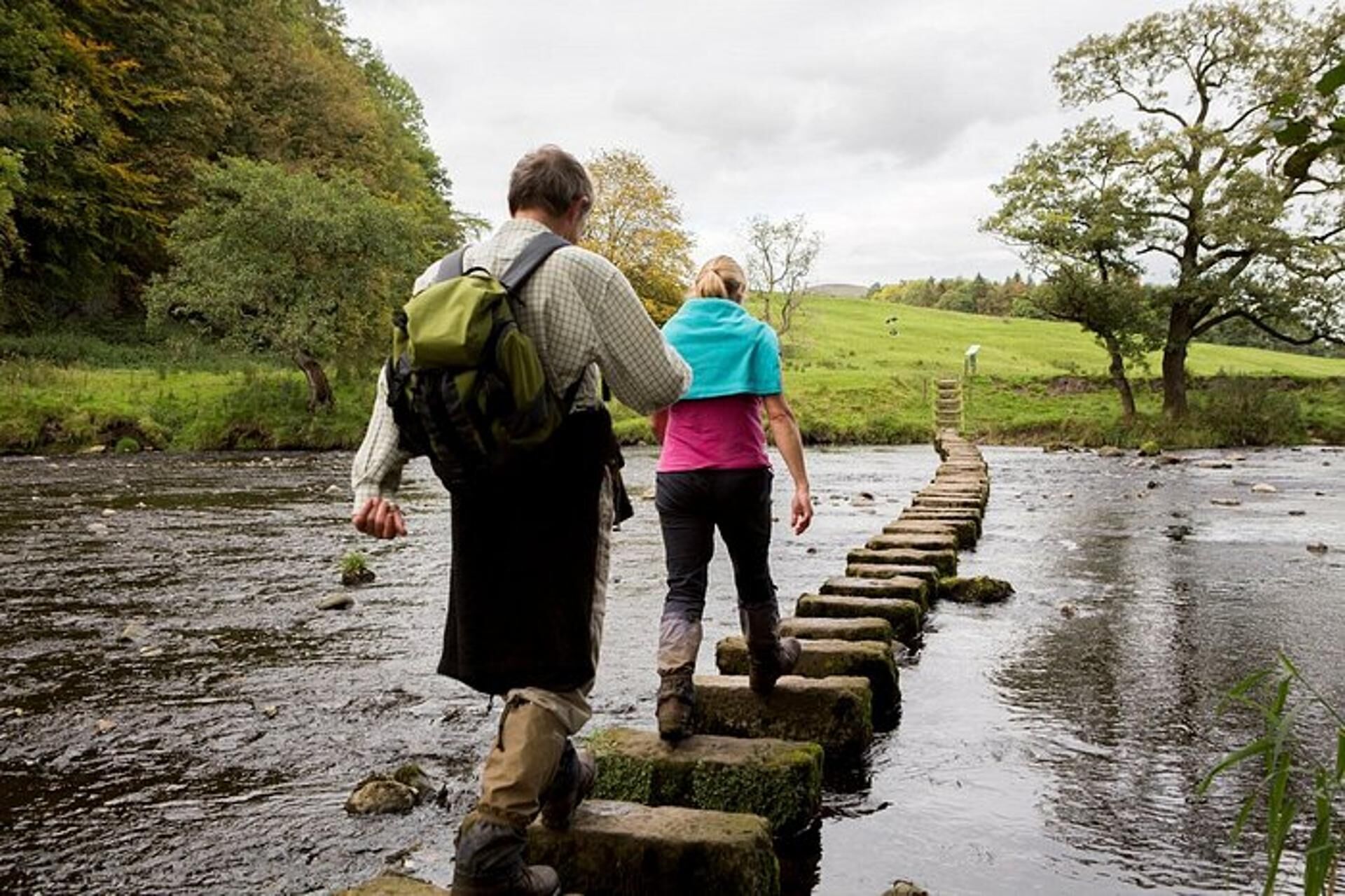 Two people crossing stepping stones over a river.