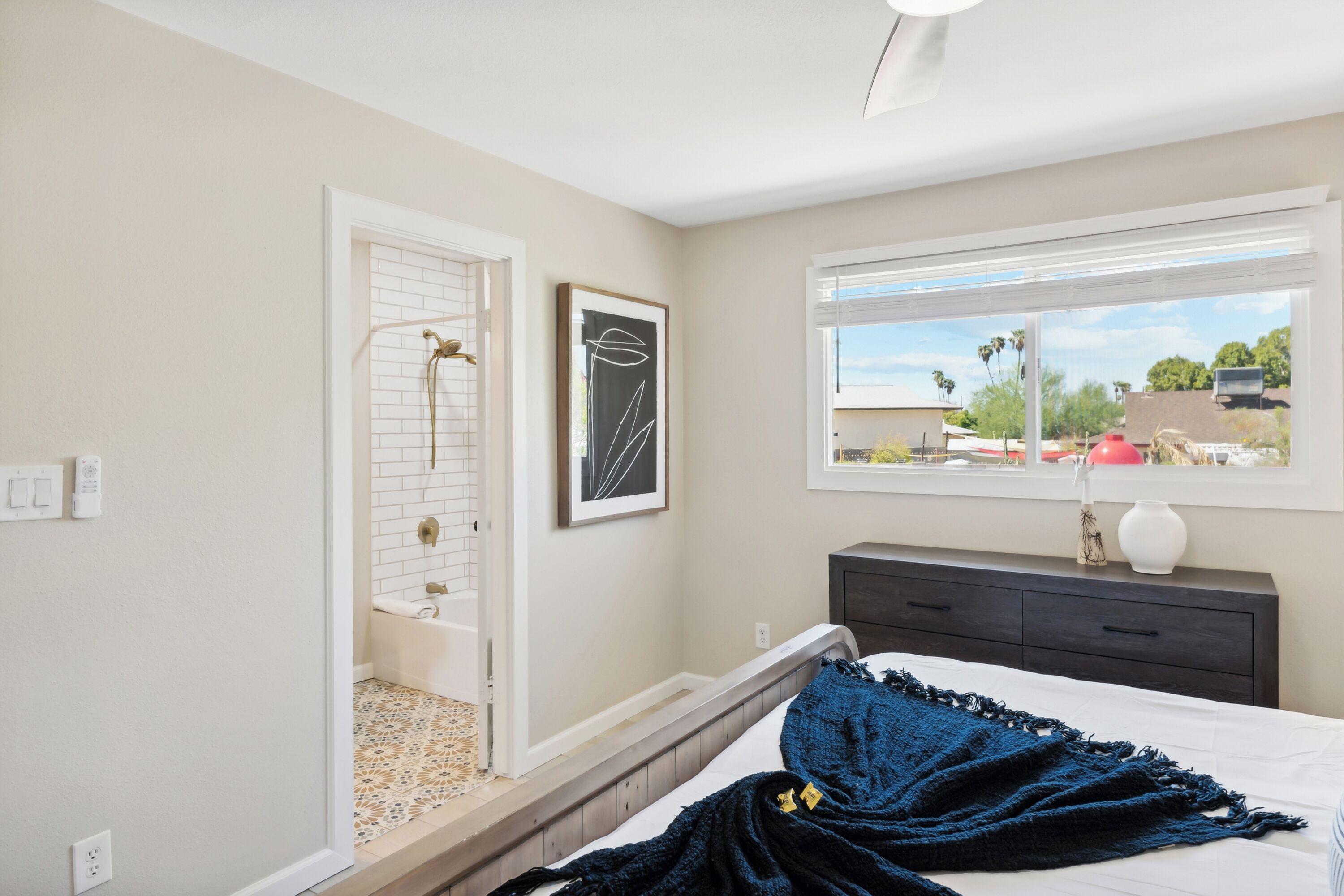 A bedroom with a bed, a window with a view, a bedside table, and a door leading to a bathroom.