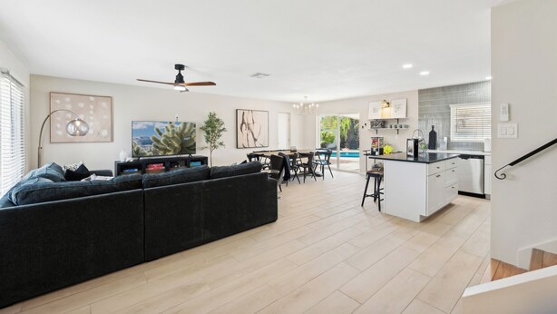 Un salon moderne avec un grand canapé de couleur foncée, un coin repas comprenant une table et des chaises, et une cuisine avec des meubles blancs et un plan de travail noir.