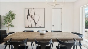 Un espace repas comprenant une table en bois, des chaises noires, un lustre, un grand tableau abstrait et une plante en pot.