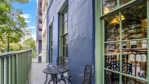 Un balcone con tavolo e sedie, una ringhiera e vista sulla strada e sugli edifici.