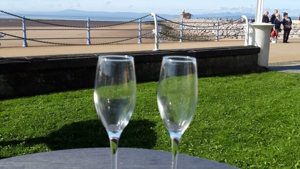 Deux verres à vin vides sont posés sur une table, offrant une vue sur une zone côtière, notamment un phare et des personnes au loin.