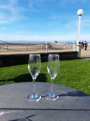 Dos copas de vino vacías sobre una mesa, con vista a la costa, incluyendo un faro y gente a lo lejos.