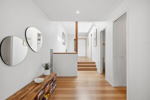 Ein moderner Flur mit Holzboden, einer Holzbank mit Pflanze und drei Wandspiegeln.