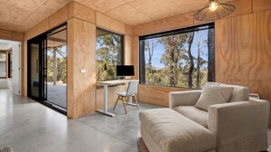 A modern interior with a wooden ceiling, a large window with a view of trees, a desk with a computer, and a sofa. - Bimbadeen Bliss (Fairhaven)