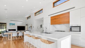 A modern kitchen with a large island, bar stools, and a dining area with a TV. - Bimbadeen Bliss (Fairhaven)