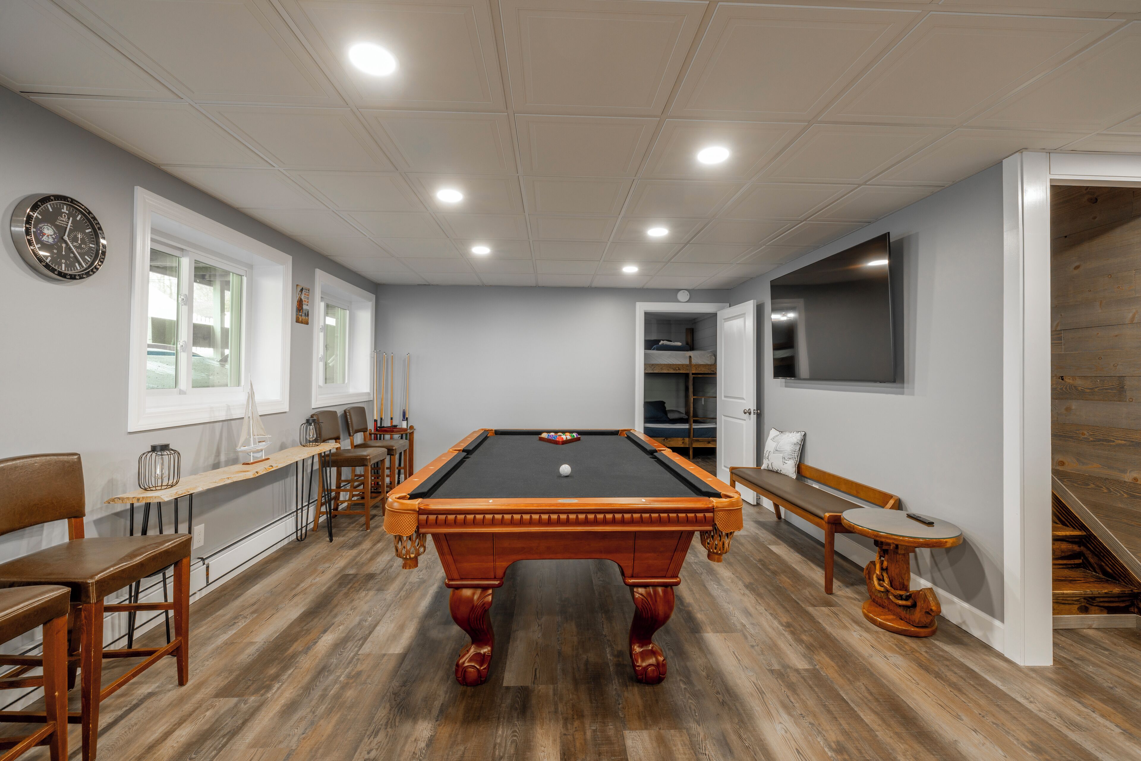 Une table de billard dans une pièce au plancher en bois, une horloge au mur et un banc.