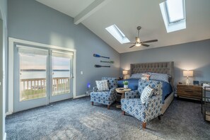 Una camera da letto con un letto grande, due poltrone, un tavolino, una ventola a soffitto e vista attraverso le porte scorrevoli in vetro.