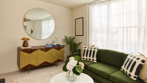 A living room with a green sofa, a round mirror, a wooden cabinet, and a vase with flowers. - The Lewes Place - Contemporary 3bdr House With Patio (Lewes)