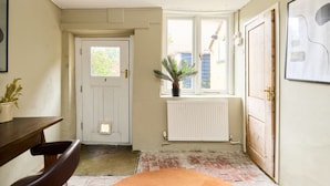 A narrow hallway with a white door, a radiator, a window with a plant, and a brown rug. - The Lewes Place - Contemporary 3bdr House With Patio (Lewes)