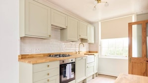 A kitchen with light green cabinets, a wooden countertop, a gas stove, an oven, and a window with a view of greenery. - The Lewes Place - Contemporary 3bdr House With Patio (Lewes)