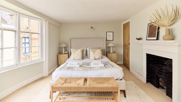 A bedroom with a large bed, bedside tables, a fireplace, and a window. - The Lewes Place - Contemporary 3bdr House With Patio (Lewes)