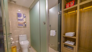 A bathroom with a toilet, a glass shower enclosure, a wooden cabinet with towels, and a framed picture on the wall. - Yi Shang Hotel Shun Ying Guang Bai (Qingyuan)