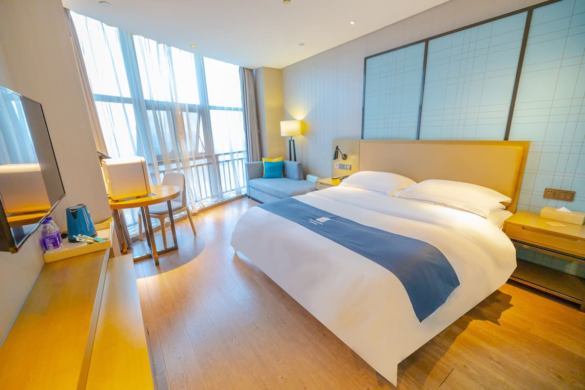 Quarto de hotel com uma cama grande, uma mesa, uma cadeira, uma televisão e uma janela com cortinas.