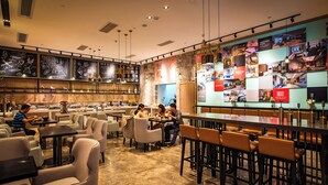 A modern cafe with multiple seating areas, including tables and chairs, and a large display wall with various images. - Yi Shang Hotel Shun Ying Guang Bai (Qingyuan)