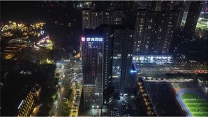 A high-rise hotel with a prominent sign, surrounded by a well-lit urban area with roads and a sports field. - Yi Shang Hotel Shun Ying Guang Bai (Qingyuan)