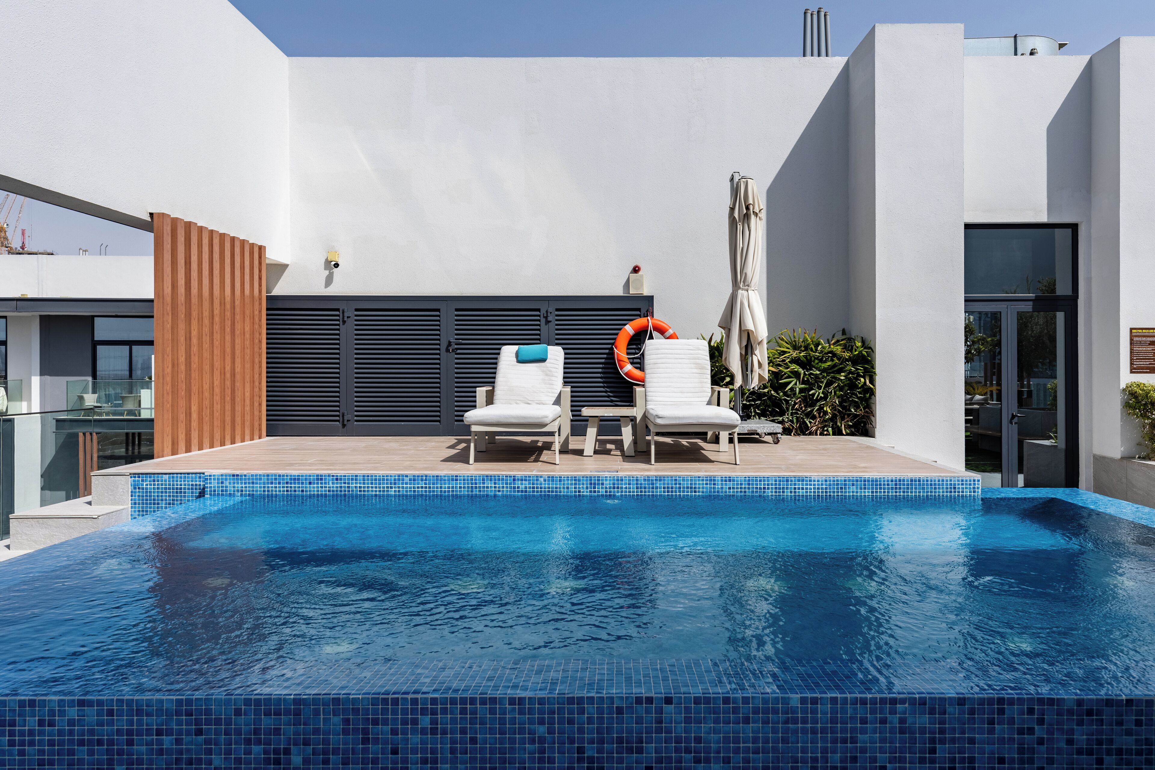 A modern outdoor pool area with two white lounge chairs and a lifebuoy.