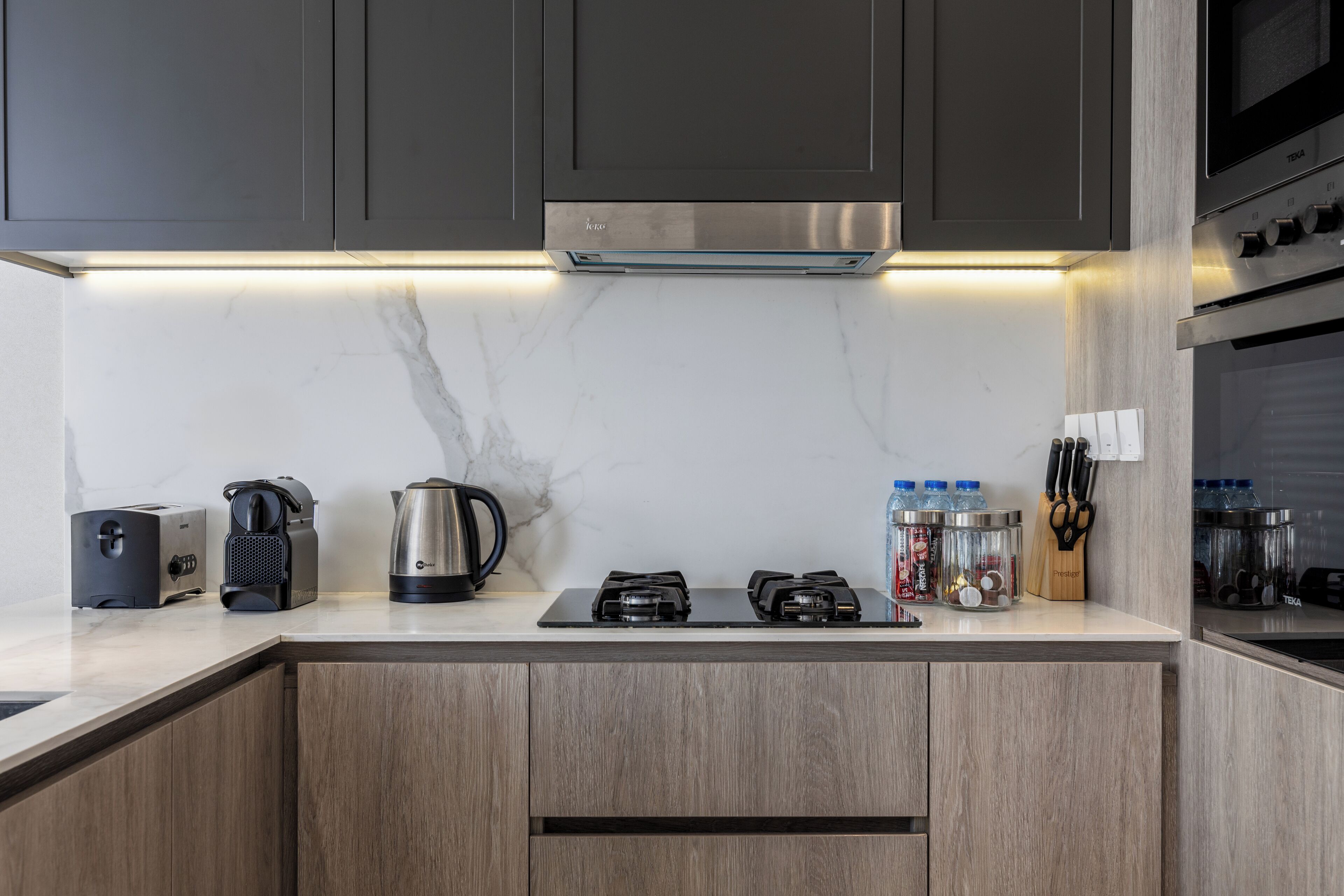 A modern kitchen with a built-in stove, a coffee maker, a kettle, and a knife block.