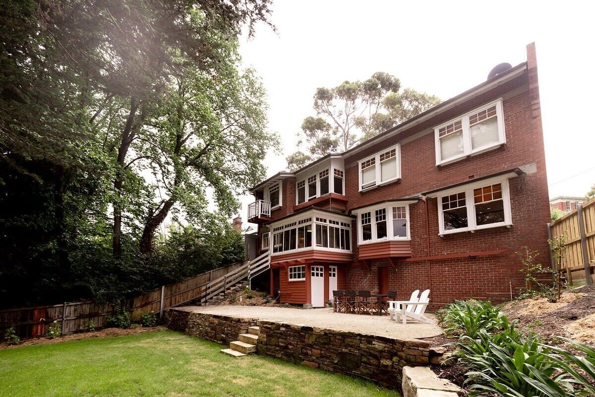 A two-story brick house with a balcony, a stone retaining wall, and a grassy backyard.
