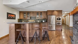 Une cuisine moderne avec des meubles en bois, des appareils en acier inoxydable et un coin bar avec des tabourets.