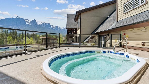 Un bain à remous avec vue sur les montagnes, une terrasse couverte et un bâtiment avec un télésiège en arrière-plan.