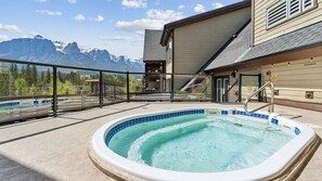 A hot tub with a mountain view, a covered deck, and a building with a ski lift in the background.