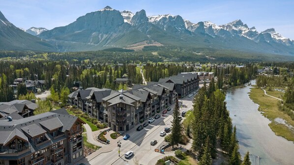 A lodge with multiple buildings, a parking area, and a river with mountains in the background.