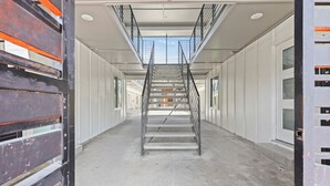 Un escalier menant au deuxième étage d’un immeuble aux murs blancs et aux grandes fenêtres.