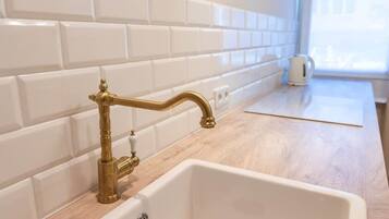 A detailed view of a brass faucet and white sink by a window. Natural light and a tiled wall elevate the kitchen design.