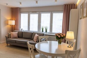 Een moderne woonkamer met een bank, een eettafel en een raam met gordijnen.