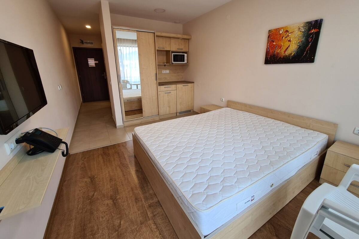 A bedroom with a bed, a TV, a phone, a microwave, and a painting.