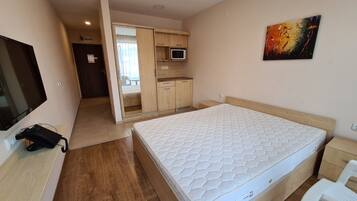A bedroom with a bed, a TV, a phone, a microwave, and a painting.