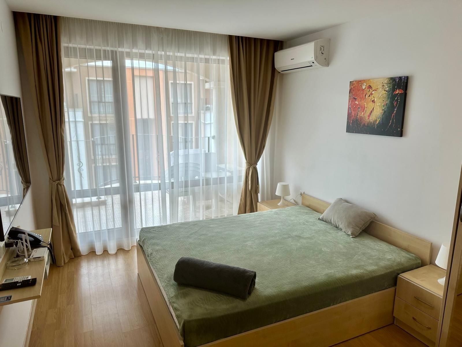 Una habitación de hotel con una cama, un escritorio con teléfono, un equipo de aire acondicionado y un cuadro en la pared.