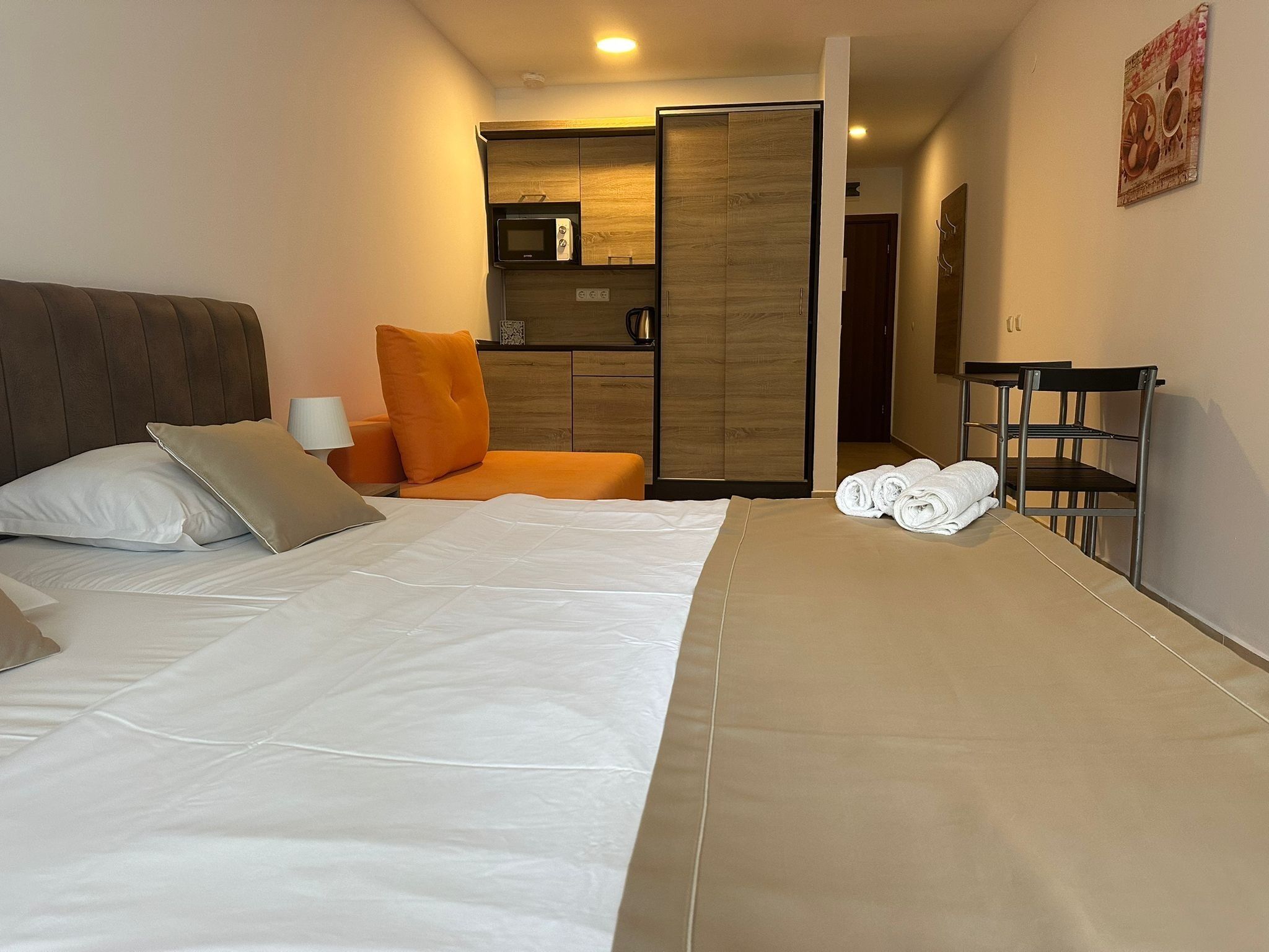 A hotel room with a bed, a sofa, a microwave, a wardrobe, and a small kitchenette.