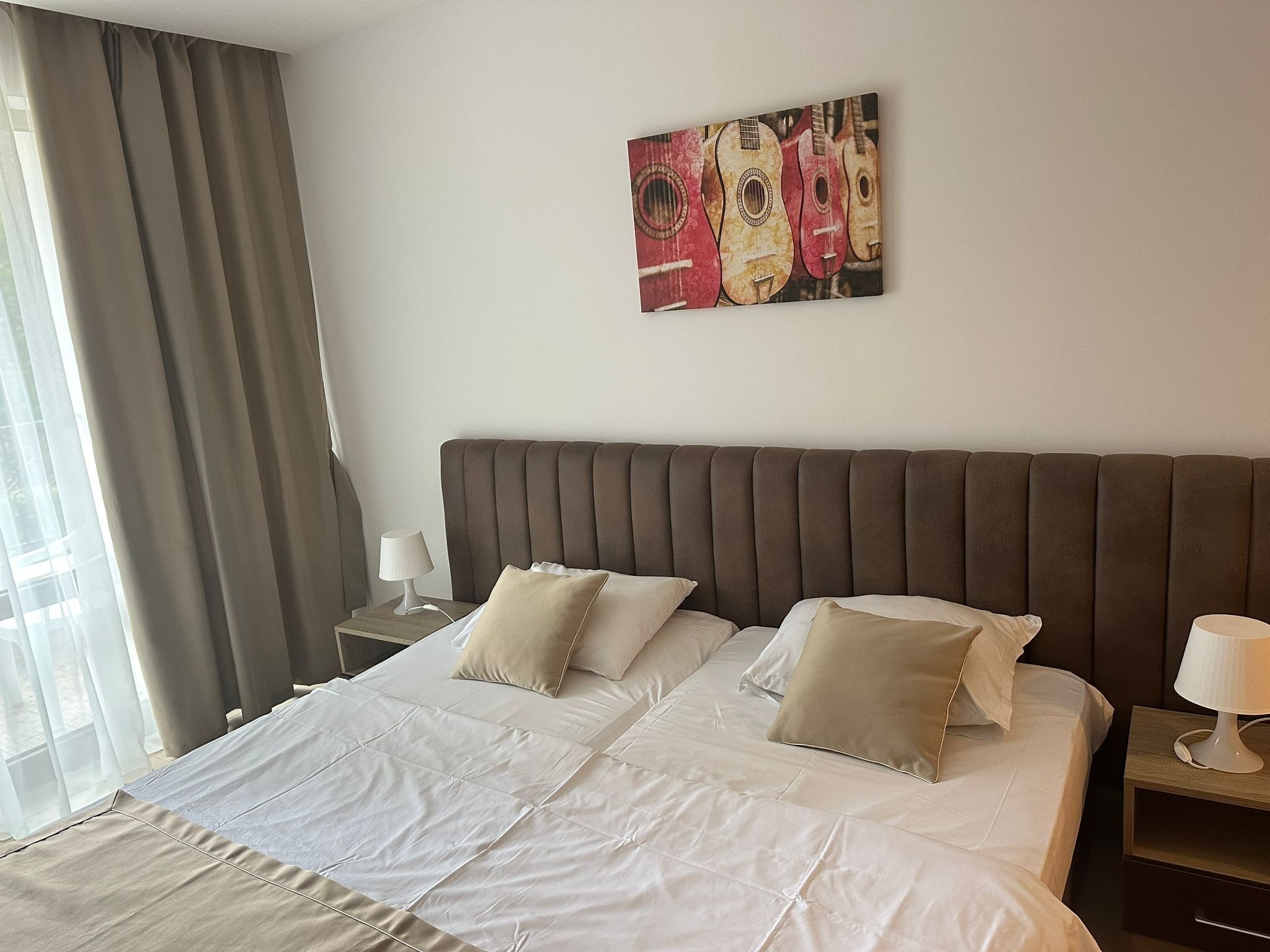 A hotel room with a large bed, two bedside tables, a headboard, and a window with curtains.
