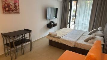 Une chambre d’hôtel avec un lit, un bureau, une chaise, une télévision et une fenêtre avec des rideaux.