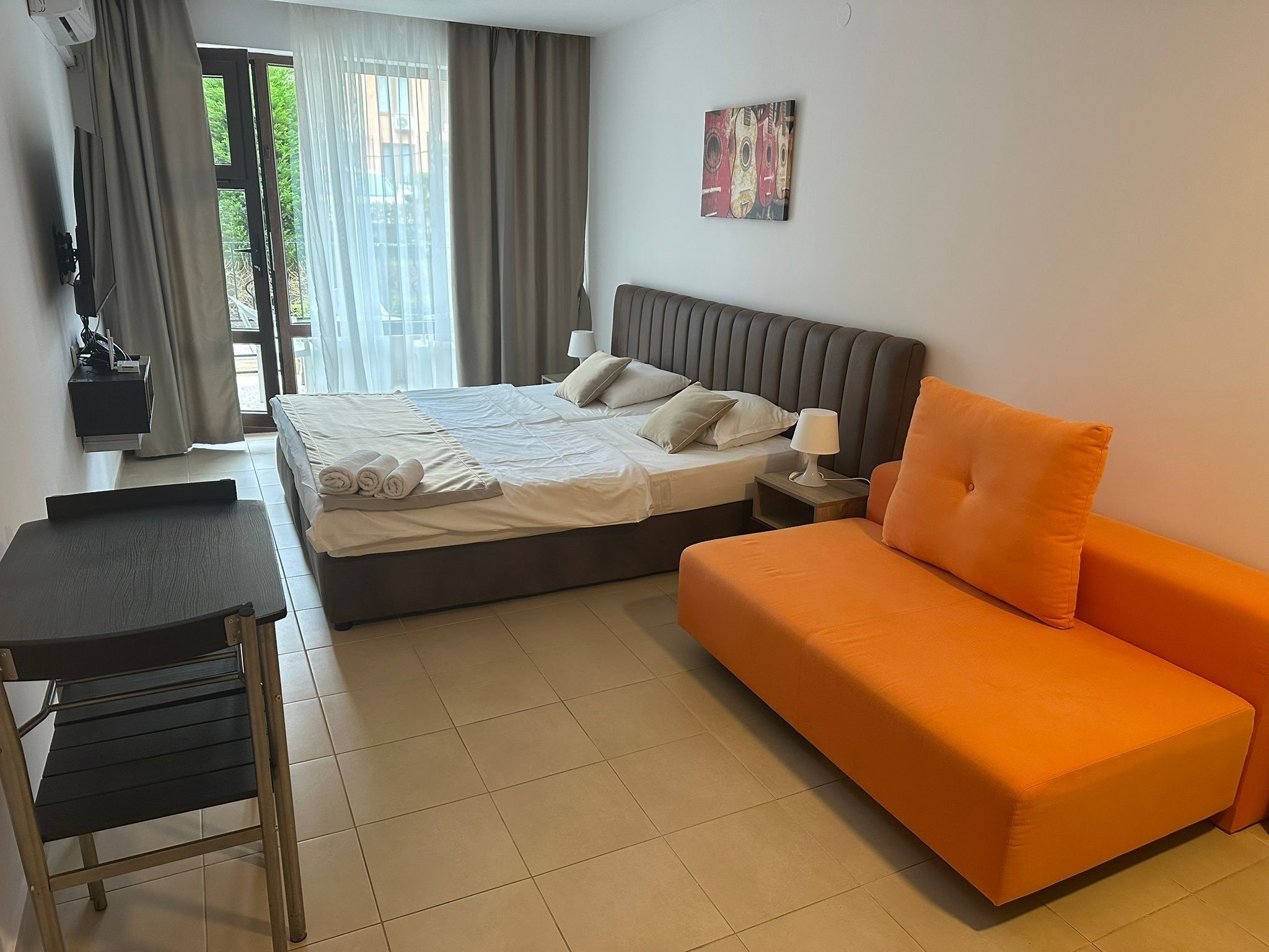 Ein Hotelzimmer mit einem Bett, einem Schreibtisch, einem orangefarbenen Sofa, einem Nachttisch und einem Bild an der Wand.