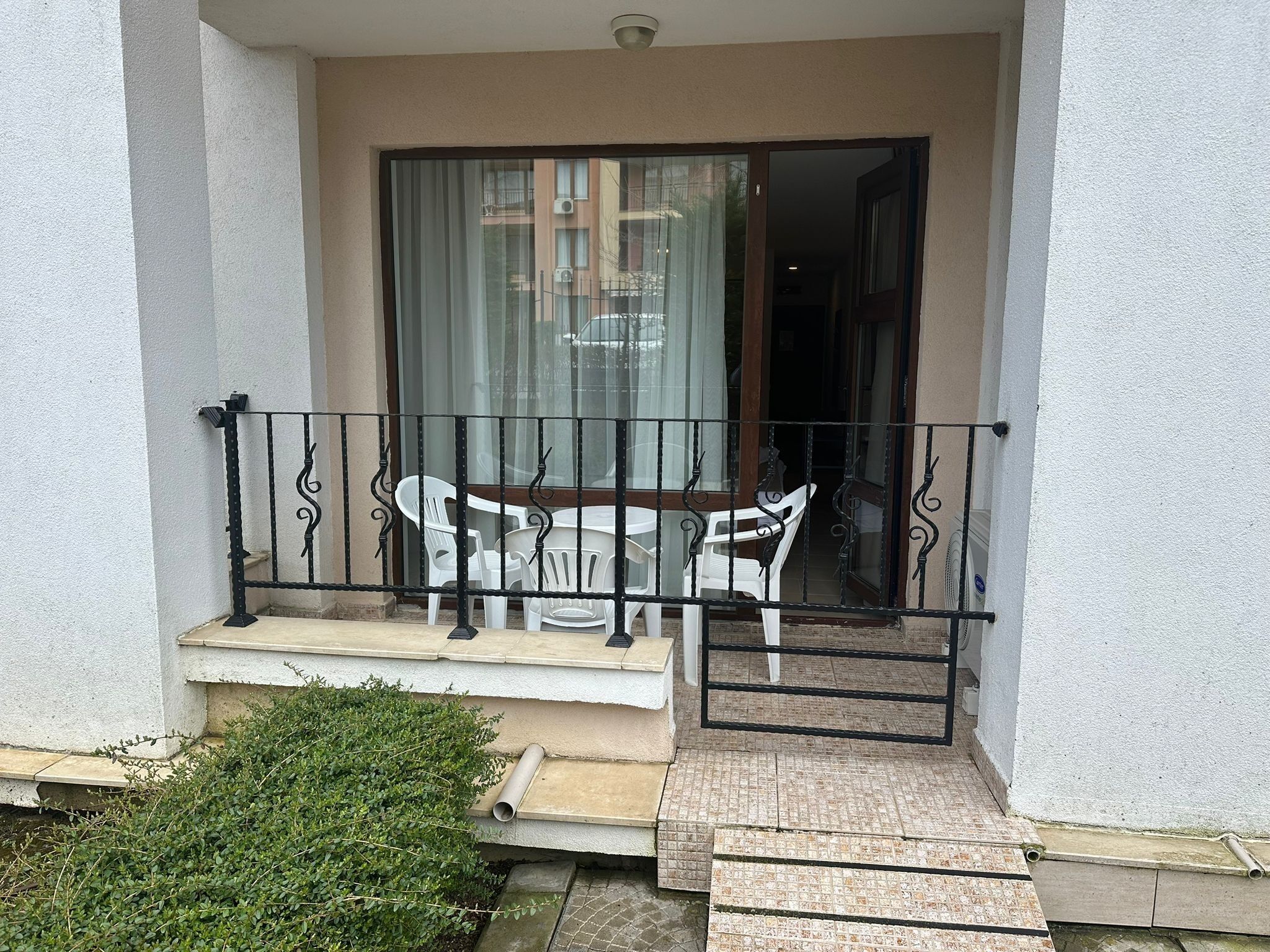 Un balcone con tavolo e sedie, un piccolo giardino e un edificio sullo sfondo.