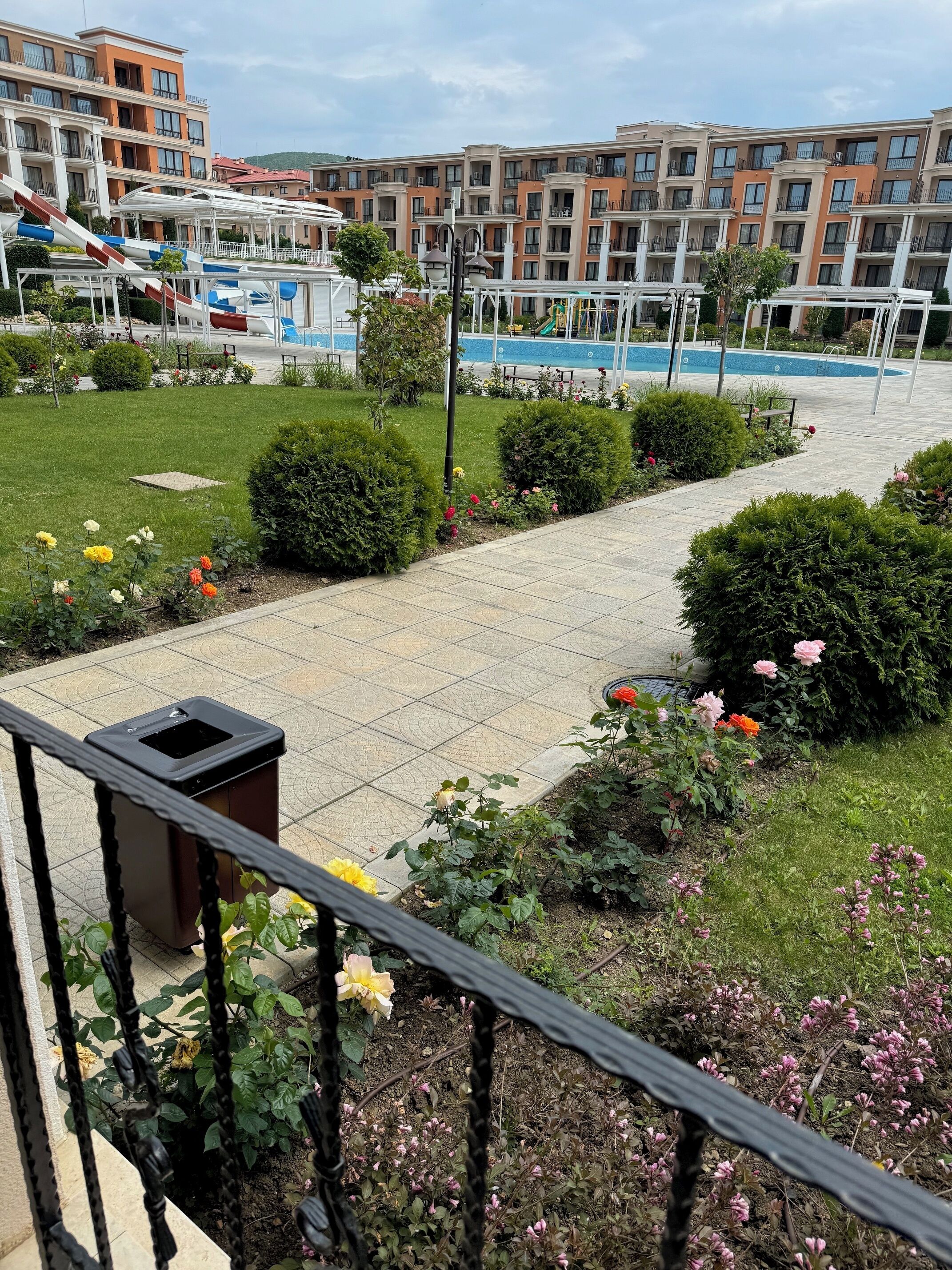 Ein Wohngebäude mit Balkonen, einem Schwimmbad und einem Gartenbereich mit Blumen und Sträuchern.