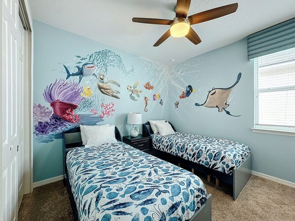 Een slaapkamer met twee bedden, een plafondventilator en een muurschildering van zeedieren.