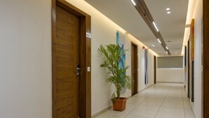 A hotel corridor with wooden doors, a potted plant, and artwork on the walls. - Hotel Aurellia (Ahmedabad)