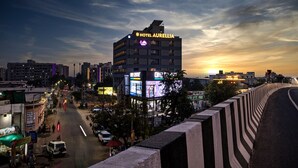 A hotel named Hotel Aurelia with a prominent sign, surrounded by a cityscape at dusk. - Hotel Aurellia (Ahmedabad)