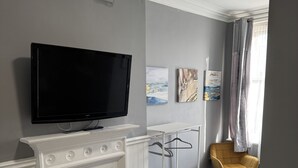A hotel room with a flat-screen TV mounted above a fireplace, a bed with a plaid bedspread, a chair, and artwork on the walls. - Holystone Bar and Restaurant  (Newcastle-upon-Tyne)